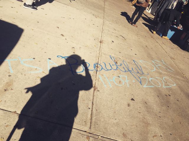 My shadow falls over a sidewalk where someone has painted 'It's a BEAUTIFUL day' the day the 2020 election was won by Biden
