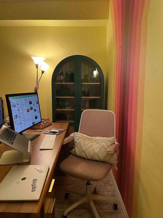 A view down the side of a wooden desk. A rainbow is barely visible on the wall, and the camera faces a teal display cabinet.