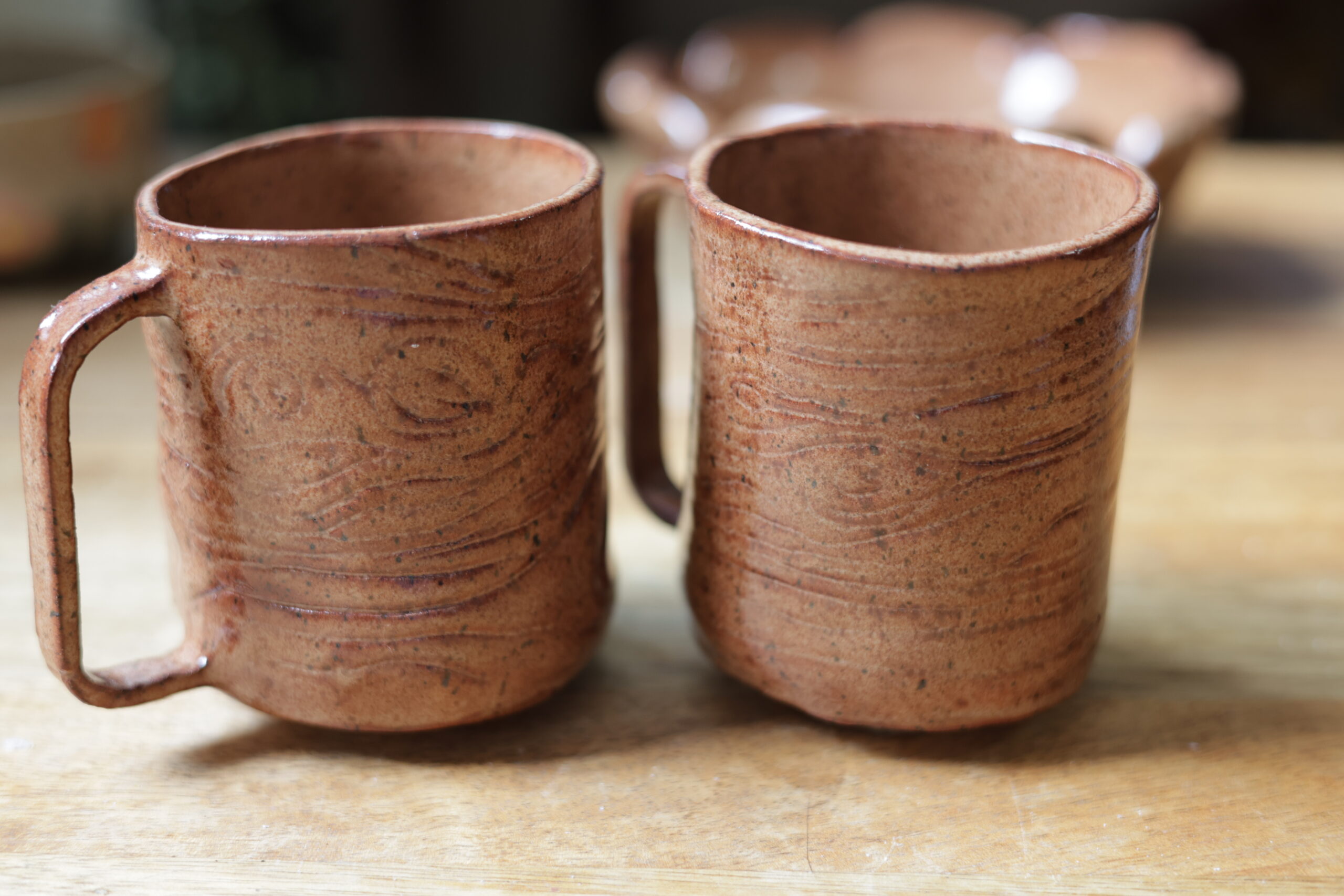 Two slab-built ceramic mugs, light brown with a tree bark texture pressed into them.